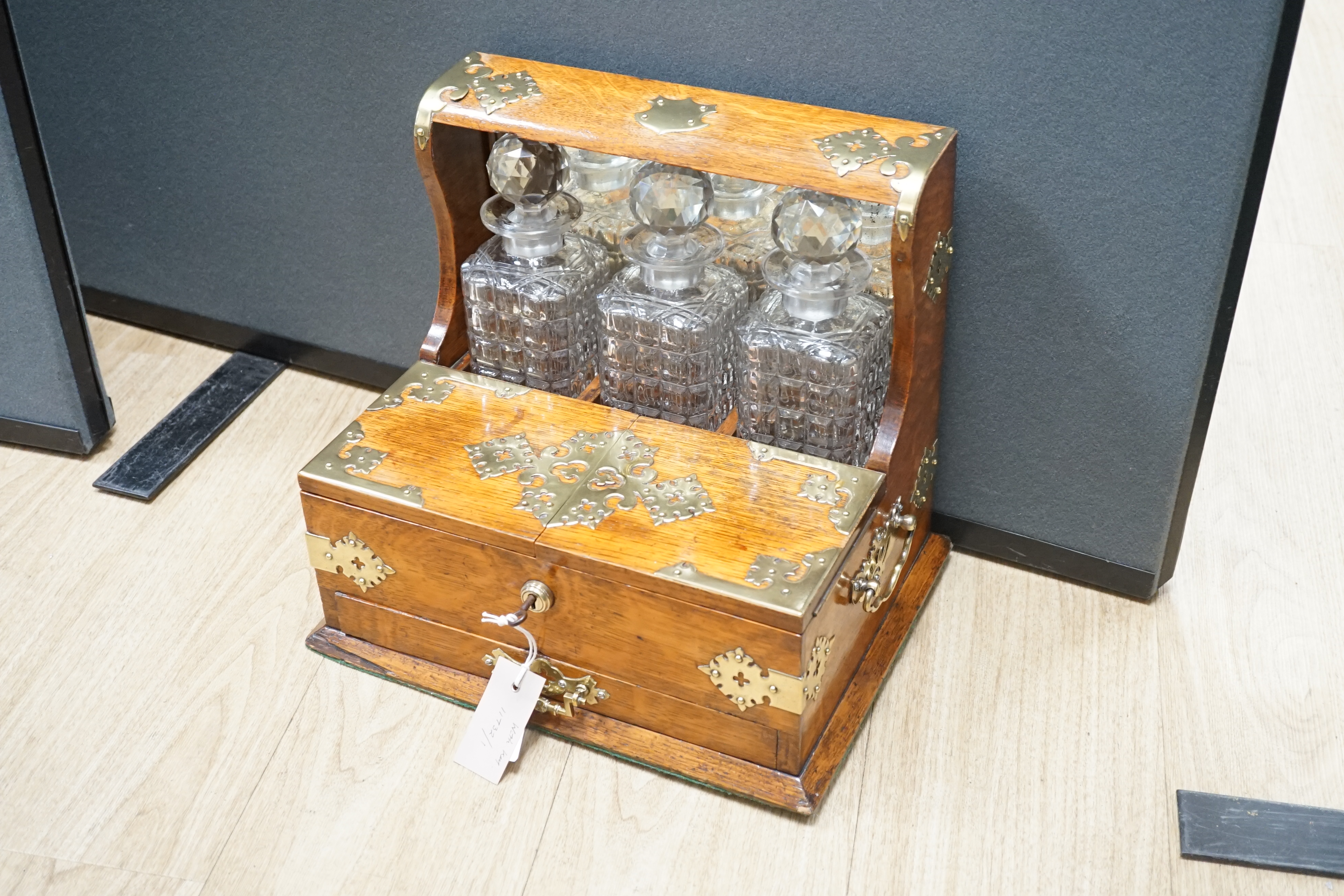 A Victorian oak and brass mounted three bottle tantalus, with base drawer and key, 36.5 cm wide